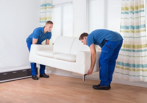 full-length-male-movers-placing-sofa-hardwood-floor-home-min